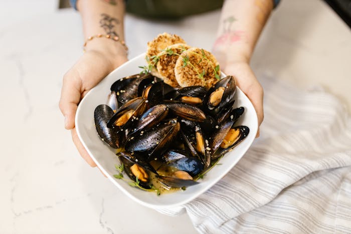 Close-up of hands holding a white plate of seasoned mussels, showcasing fresh seafood cuisine.